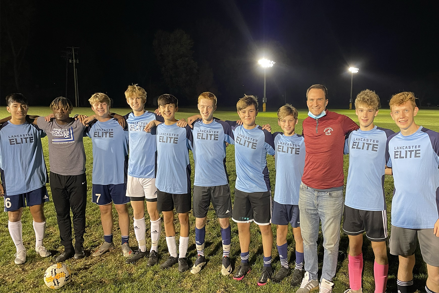 A man poses with a soccer team wearing jerseys that say Lancaster Elite