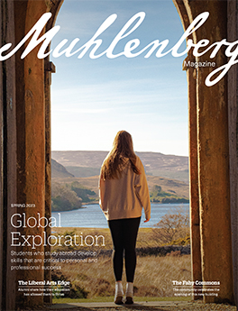 A magazine cover that says Muhlenberg Magazine with a photo of a college student looking onto a scenic vista