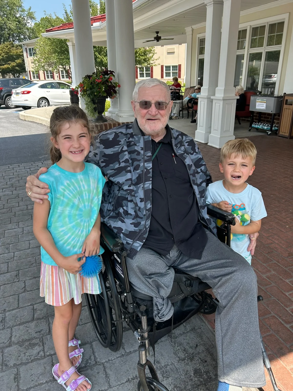 A man in a wheelchair has one arm around a young girl and one around a young boy