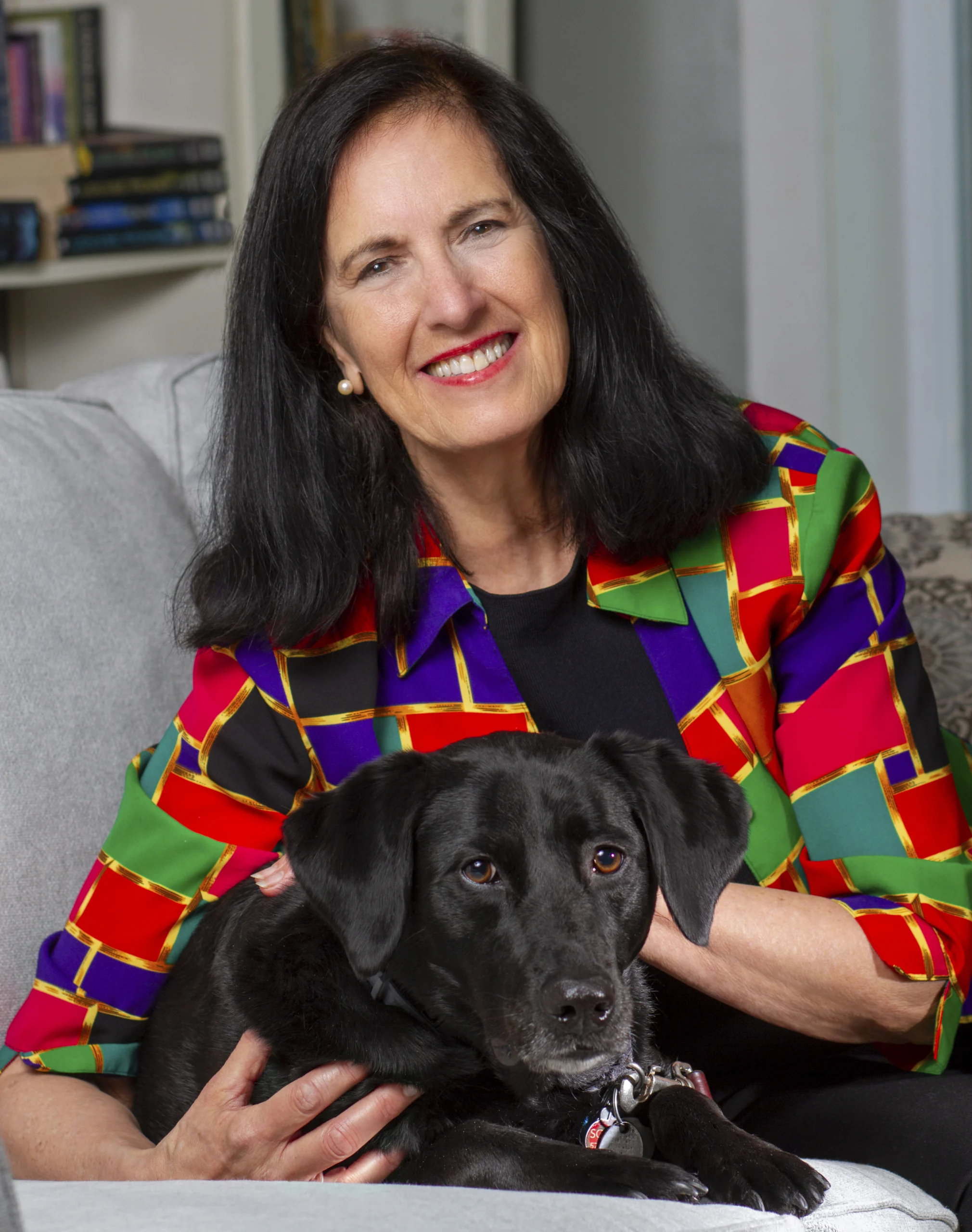 A picture of a woman in a colorful blazer with a black dog