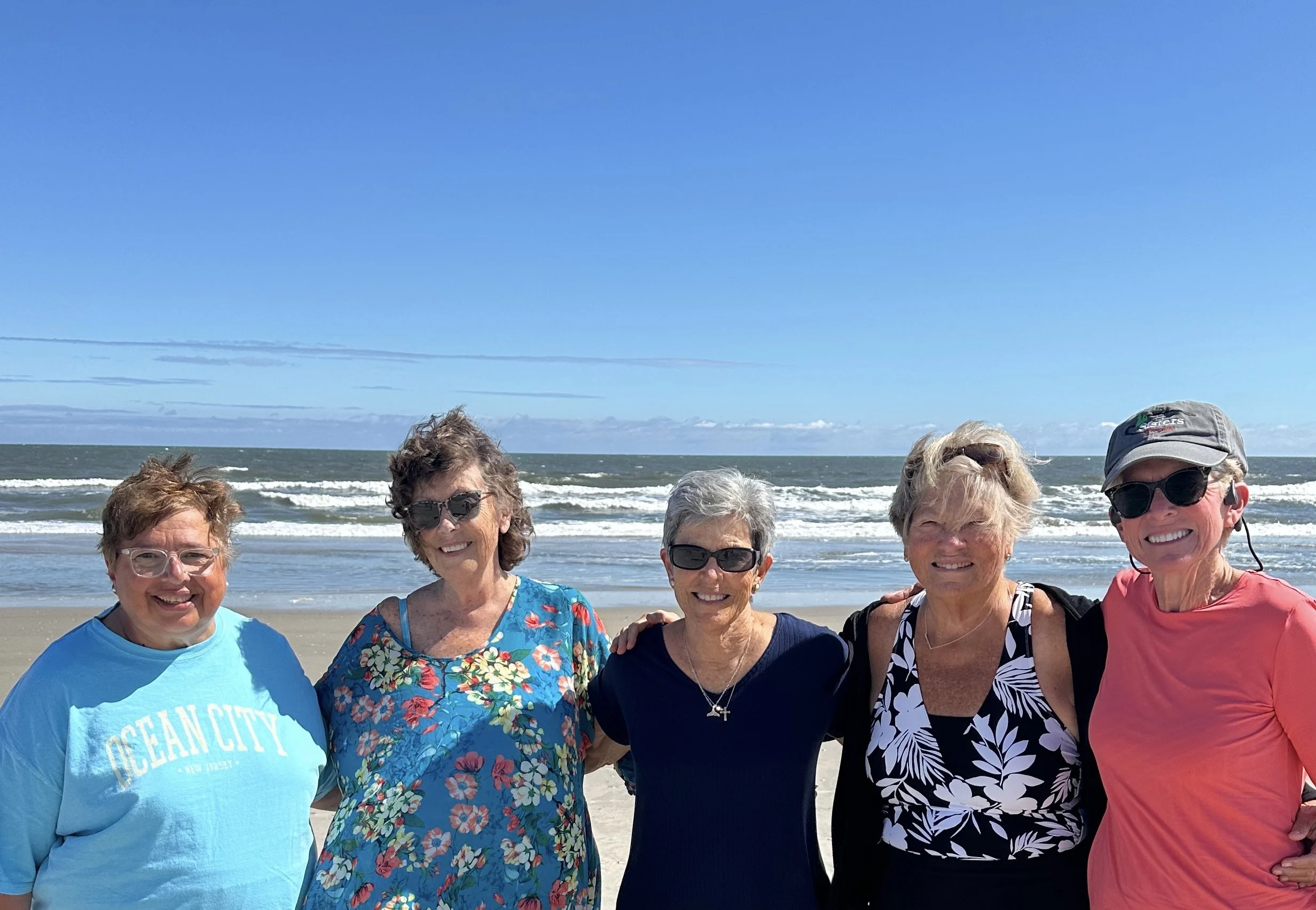 Five women stand for a photo on a beach