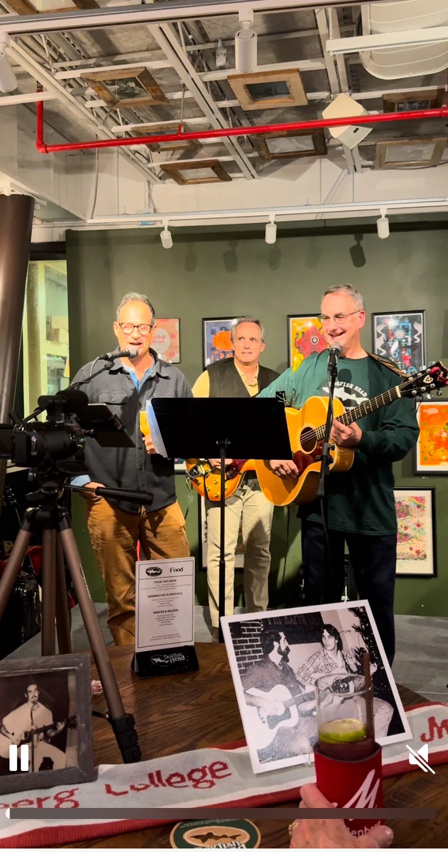 Three men sing on a stage at a brewery