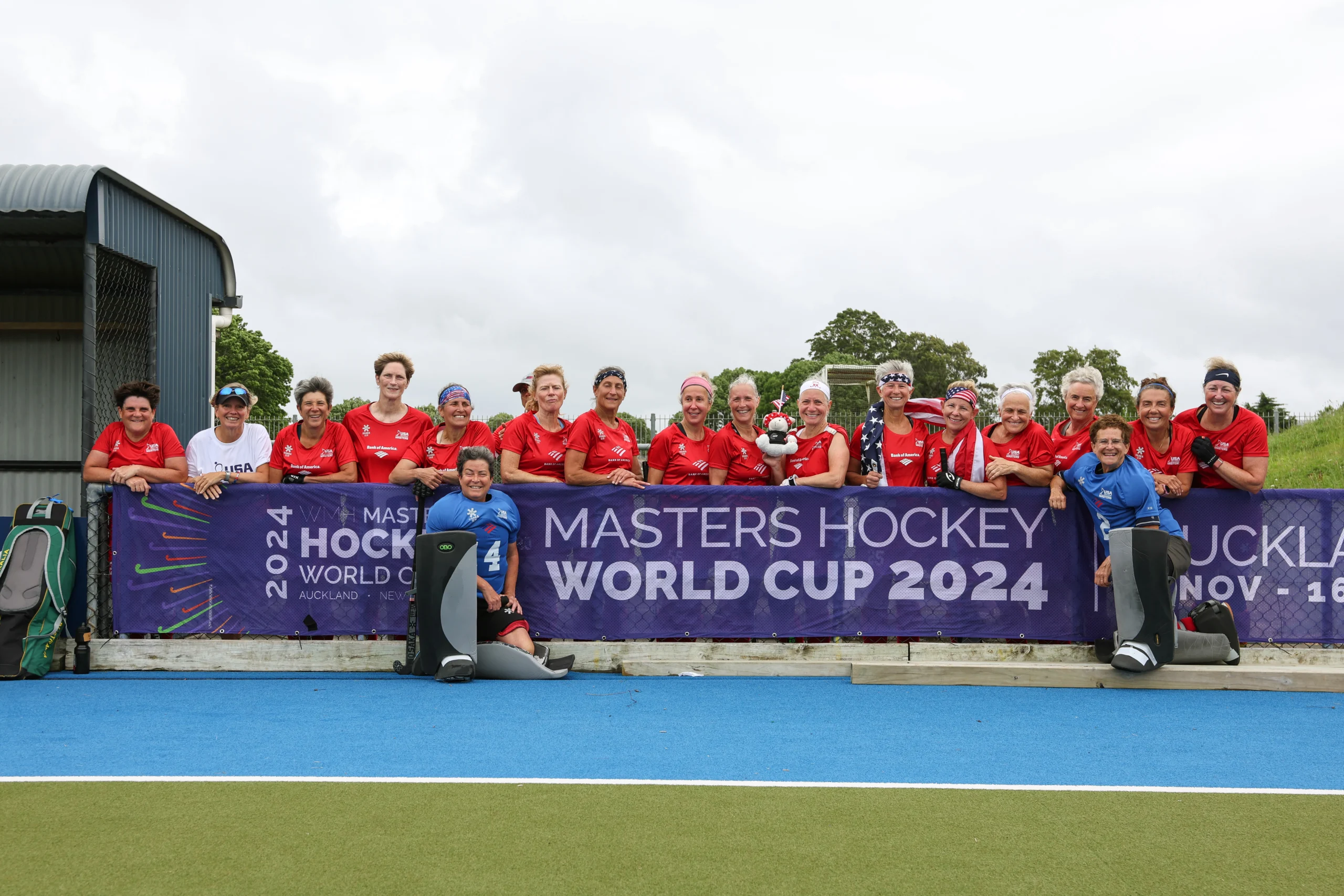 A group of field hockey players in front of a banner that says Masters Hockey World Cup 2024