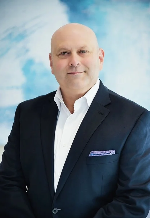 A headshot of a man in a white shirt and blue blazer