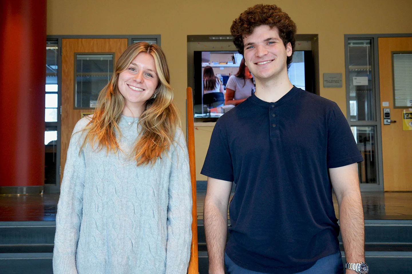 Two college students smile together for a photo inside a science building