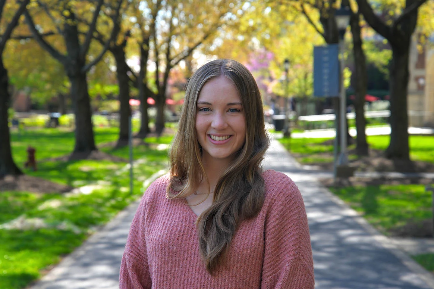 A headshot of a college student with long hair with Academic Row in the background