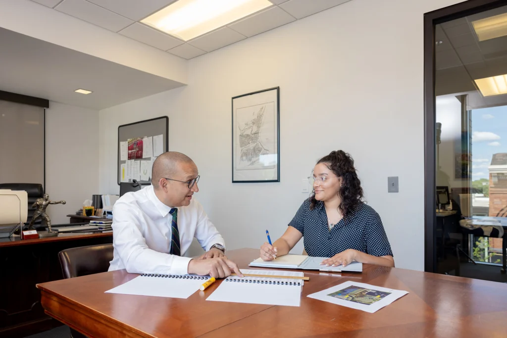 Two people work at a table with notebooks and printouts in front of them